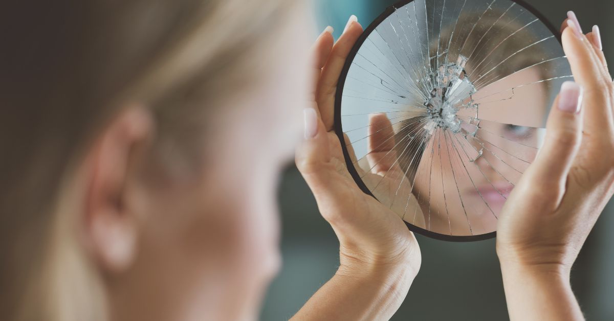 Woman looking into cracked mirror